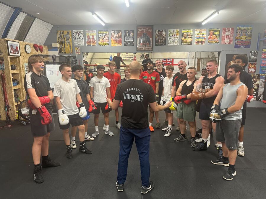 Coach addressing a circle of junior and senior boxers wearing red gloves before training